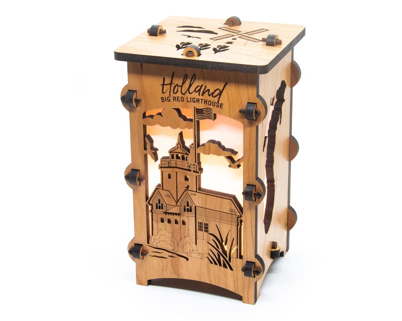 Puede incluir: L&aacute;mpara de madera con un dise&ntilde;o recortado del Big Red Lighthouse en Holland, Michigan. La l&aacute;mpara est&aacute; iluminada desde el interior, creando un brillo c&aacute;lido. El texto "Holland Big Red Lighthouse" est&aacute; grabado en la parte delantera de la l&aacute;mpara.