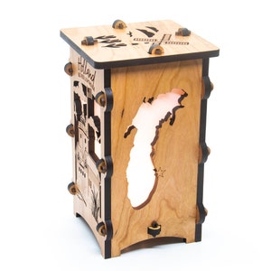 Puede incluir: Una l&aacute;mpara de madera con un recorte del estado de Michigan. La l&aacute;mpara est&aacute; hecha de madera de cerezo y tiene un acabado negro. La l&aacute;mpara est&aacute; encendida y la luz brilla a trav&eacute;s del recorte del estado. La l&aacute;mpara tiene un peque&ntilde;o molino de viento en la parte superior y las palabras "Holland, MI" en el lateral.