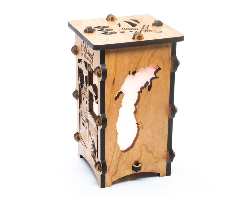 Puede incluir: Una l&aacute;mpara de madera con un recorte del estado de Michigan. La l&aacute;mpara est&aacute; hecha de madera de cerezo y tiene un acabado negro. La l&aacute;mpara est&aacute; encendida y la luz brilla a trav&eacute;s del recorte del estado. La l&aacute;mpara tiene un peque&ntilde;o molino de viento en la parte superior y las palabras "Holland, MI" en el lateral.
