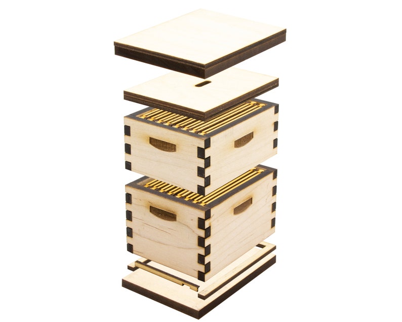 Puede incluir: Una colmena de madera desmontada con un acabado de madera clara y detalles negros. La colmena est&aacute; compuesta por una base, dos cajas, una tapa y una cubierta superior. Las cajas tienen una serie de peque&ntilde;os marcos dorados en el interior.