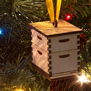 May include: A wooden beehive ornament with a yellow ribbon for hanging on a Christmas tree.