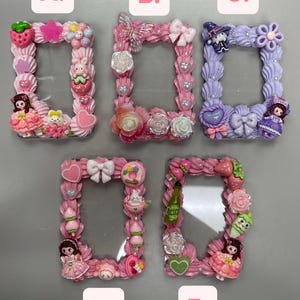 May include: A collection of five decorative picture frames. Each frame is rectangular with a pink, textured border. The frames are adorned with various embellishments, including miniature figurines, bows, strawberries, and flowers. The frames are labeled A, B, C, D, and E.