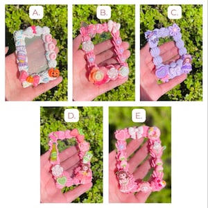 Puede incluir: Una colección de cinco marcos de fotos decorativos, cada uno con un diseño único. Los marcos están adornados con varios adornos, incluyendo lazos, flores y figuras en miniatura. Los marcos se sostienen en una mano sobre un fondo verde.