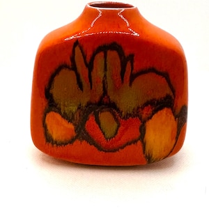 May include: A small, orange ceramic vase with a square base and rounded top. The vase features a floral design in shades of brown, yellow, and red. The glossy finish enhances the vibrant colours and intricate details of the artwork.