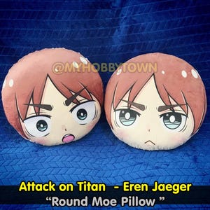 以下が含まれることがあります： アニメキャラクターの顔が描かれた丸いクッションが2つ。クッションは赤褐色で、黒い目と白いハイライトが入っています。クッションの下には「Attack on Titan - Eren Jaeger」と「Round Moe Pillow」の文字が印刷されています。