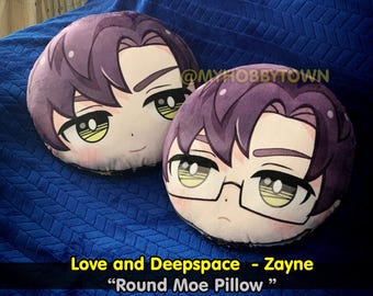 May include: Two round plush pillows with anime-style faces. The pillow on the left has purple hair and brown eyes. The pillow on the right has purple hair, brown eyes, and glasses. The text "Love and Deep Space - Zane" and "Round Moe Pillow" is printed below the pillows.