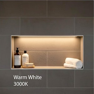 May include: A recessed bathroom shelf with warm white lighting. The shelf contains two bottles of soap, a bar of soap on a wooden tray, and a rolled-up white towel. The text "Warm White 3000K" is displayed.