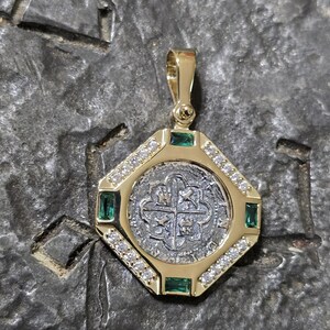 May include: A gold pendant featuring a silver coin at its center, surrounded by a gold frame. The frame is adorned with emeralds and diamonds. The pendant has a bail for attaching to a chain.