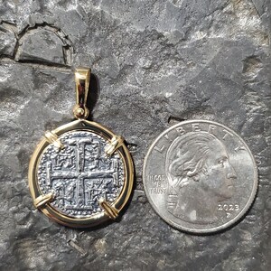 Puede incluir: Un colgante de moneda de oro y plata con un dise&ntilde;o de cruz. La moneda est&aacute; rodeada por un marco de oro y tiene un asa para sujetar a una cadena. La moneda es aproximadamente del tama&ntilde;o de una moneda de 25 centavos de d&oacute;lar estadounidense.