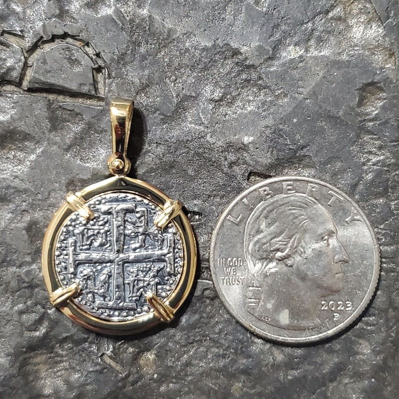 Puede incluir: Un colgante de moneda de oro y plata con un dise&ntilde;o de cruz. La moneda est&aacute; rodeada por un marco de oro y tiene un asa para sujetar a una cadena. La moneda es aproximadamente del tama&ntilde;o de una moneda de 25 centavos de d&oacute;lar estadounidense.