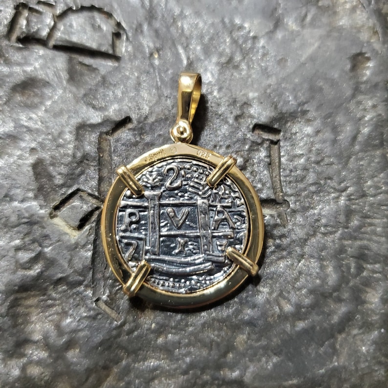 Puede incluir: Un colgante de oro con una r&eacute;plica de plata de una moneda espa&ntilde;ola de 2 reales con la inscripci&oacute;n "P.V.A." y el a&ntilde;o "1728".