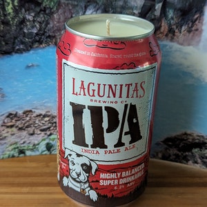 May include: A red and white Lagunitas Brewing Co. IPA beer can candle. The candle features the IPA logo, a dog illustration, and text that reads "India Pale Ale" and "Highly Balanced Super Drinkable 6.2% ABV".