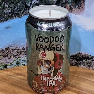 May include: A candle in a repurposed beer can. The can is green and silver with the words "Voodoo Ranger Imperial IPA" and a skull graphic. The candle has a white wax and a single wick.