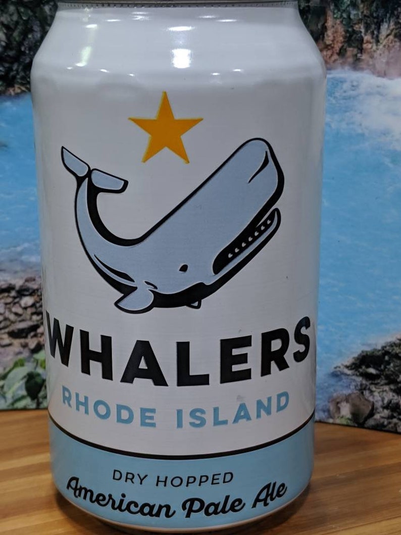 May include: A white beer can with a blue whale illustration and a yellow star. The can reads "Whalers Rhode Island" and "American Pale Ale". The can has a light blue band at the bottom.