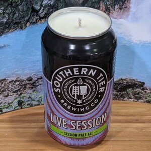 May include: A black candle in a beer can from Southern Tier Brewing Co. The can features the text "Southern Tier Brewing Co. Live Session Session Pale Ale". The candle has a white wax and a wick.