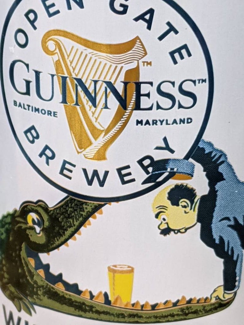 May include: A Guinness Brewery advertisement featuring the Guinness logo with a harp and the text "Baltimore Maryland". The image includes a cartoon of a man and an alligator with a glass of beer.