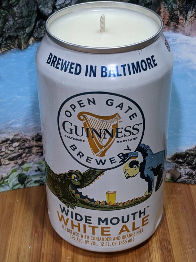 May include: A white candle in a repurposed Guinness beer can. The can features the text "BREWED IN BALTIMORE" and "OPEN GATE GUINNESS BREWER". The label also reads "WIDE MOUTH WHITE ALE" and "12 fl oz (355 ml)".