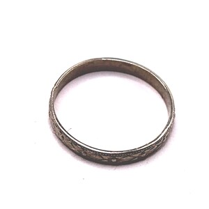 May include: A silver-toned ring with an intricate floral pattern. The ring is circular and appears to be made of metal. The floral design is etched around the band, adding detail to the jewelry. The ring is set against a white background.