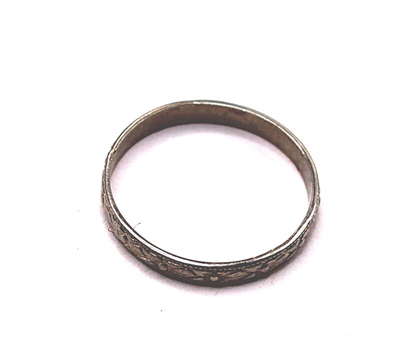 May include: A silver-toned ring with an intricate floral pattern. The ring is circular and appears to be made of metal. The floral design is etched around the band, adding detail to the jewelry. The ring is set against a white background.