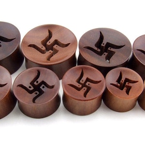 May include: Set of eight wooden ear gauges with a carved swastika design. The gauges are various sizes and are a dark brown colour.