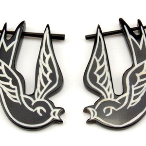 Może przedstawiać: Para czarno-białych kolczyków z rogu w kształcie lecącego jaskółki. Kolczyki są wykonane z rogu i mają biały kontur.