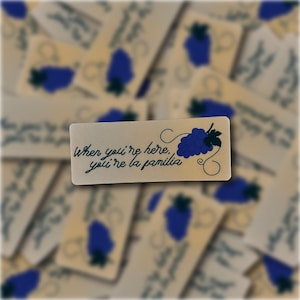 May include: A beige sticker with blue grapes and the text "When you're here, you're la familia."