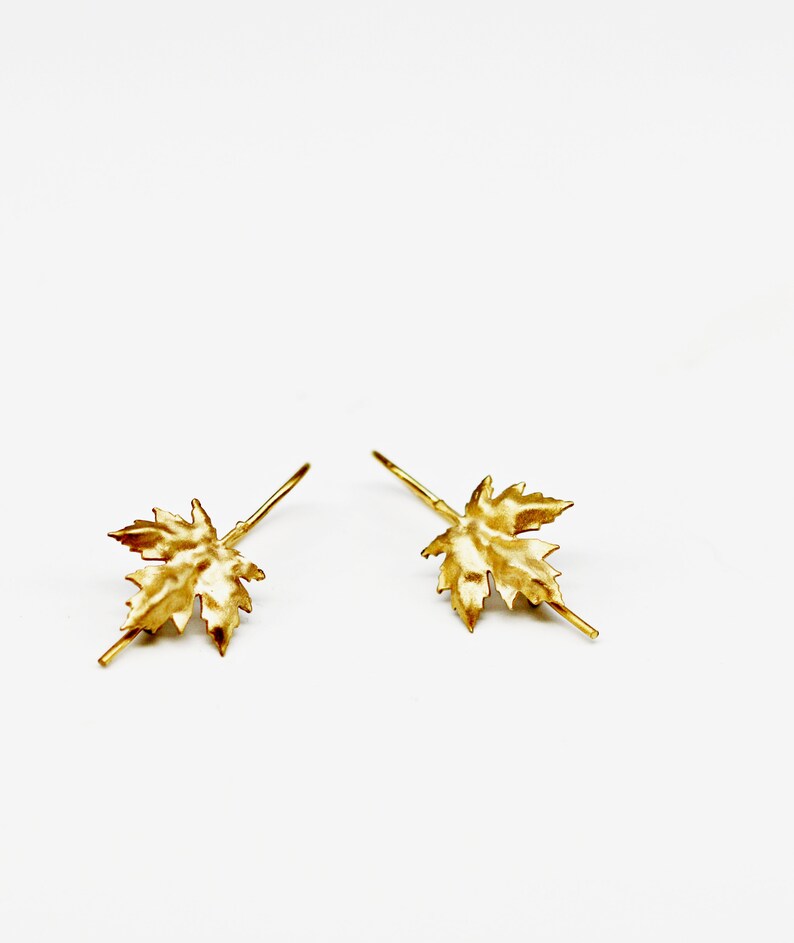 May include: A pair of gold-toned earrings with a maple leaf design.