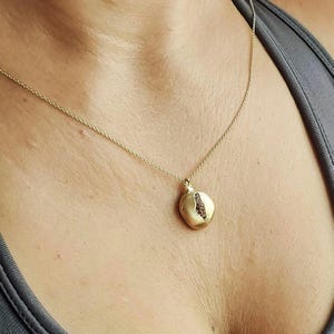 Puede incluir: Un collar de cadena de oro con un colgante de granada. El colgante est&aacute; hecho de oro y tiene una piedra preciosa roja en su interior.