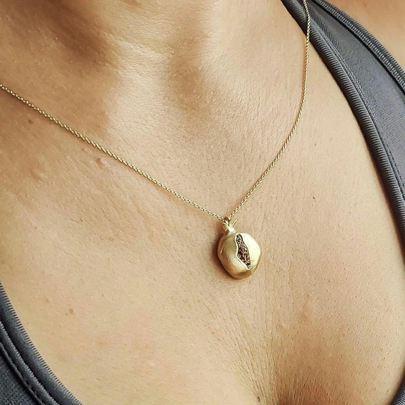 Puede incluir: Un collar de cadena de oro con un colgante de granada. El colgante est&aacute; hecho de oro y tiene una piedra preciosa roja en su interior.