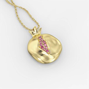 Puede incluir: Un collar de oro con un colgante de granada. El colgante est&aacute; decorado con piedras preciosas rosas.