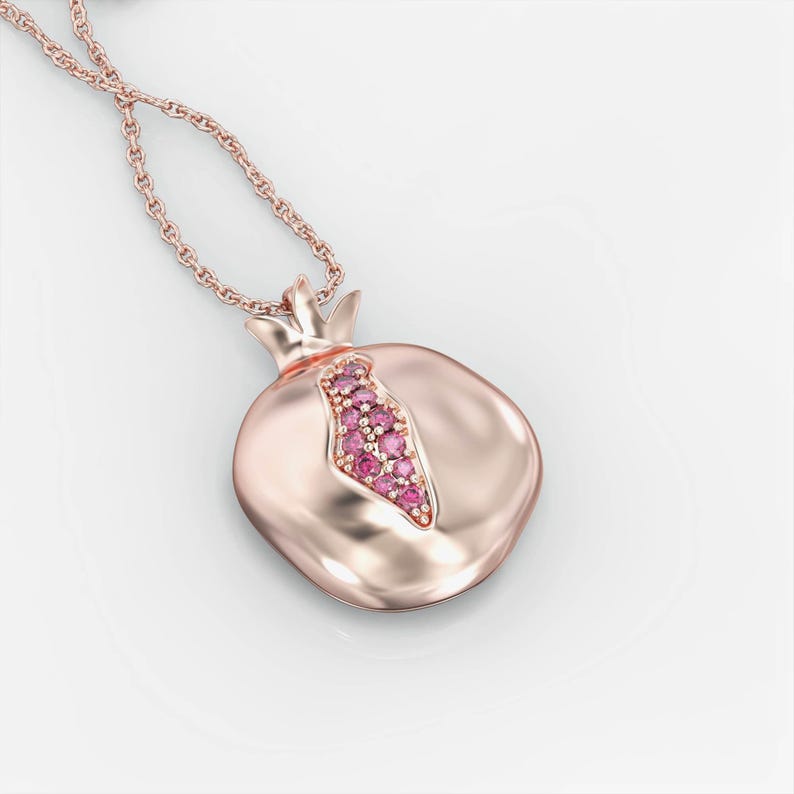 Puede incluir: Un collar de oro rosa con un colgante de granada. El colgante est&aacute; decorado con piedras preciosas rosas.