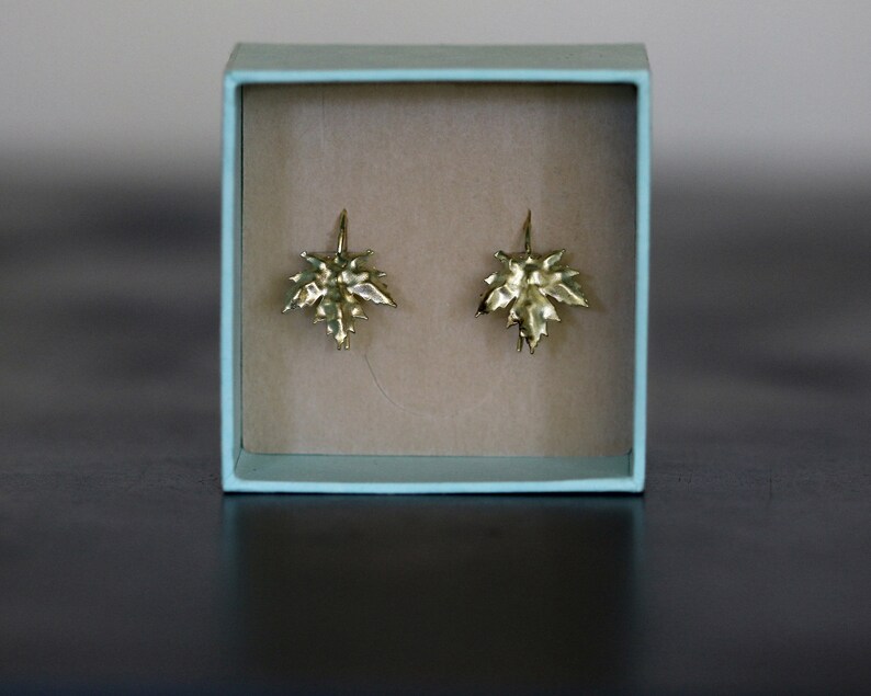 May include: A pair of gold maple leaf earrings in a light blue box.