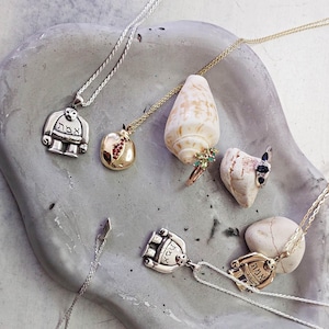 Puede incluir: Una colecci&oacute;n de collares de plata y oro con colgantes que presentan texto hebreo, una granada y una concha. Los collares se muestran sobre una superficie gris texturizada.