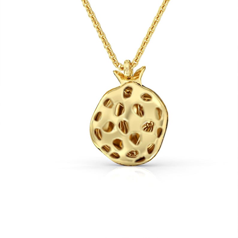 Puede incluir: Un collar dorado con un colgante de granada detallado. El colgante est&aacute; hecho de metal texturizado y tiene un dise&ntilde;o hueco.