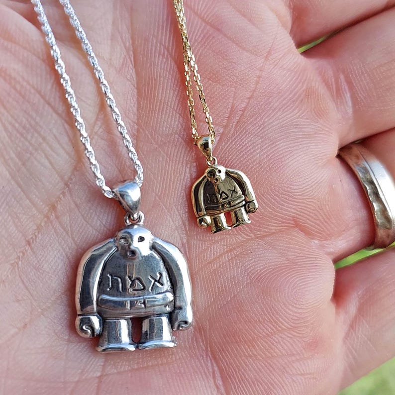 Puede incluir: Dos collares de plata y oro con colgantes que representan una figura de dibujos animados con la palabra "אדם" escrita en el pecho. La figura lleva un sombrero y una barba.