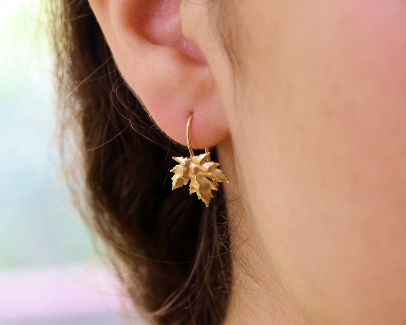 May include: Gold earrings with a leaf design. The leaves are textured and have a slightly hammered look.
