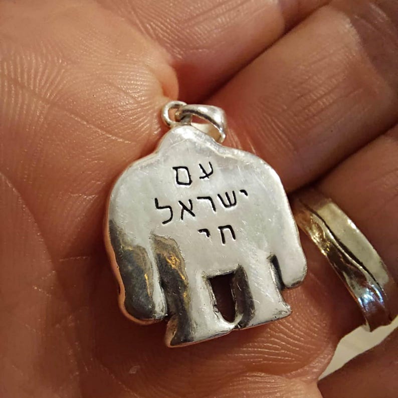 Puede incluir: Pendiente de plata con forma de persona con las palabras hebreas "Chai" y "Shema Yisrael" inscritas en la parte delantera.