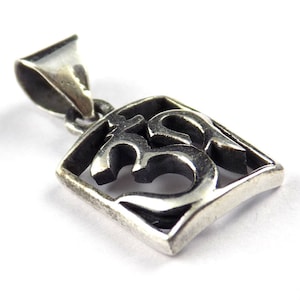 May include: A silver-colored pendant featuring the Om symbol within a square frame. The pendant has a bail for a chain and is set against a white background. The Om symbol is a sacred sound and spiritual icon.