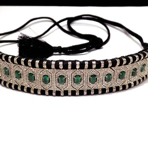 Peut inclure: Un collier ras du cou argenté orné de pierres précieuses vert émeraude et de pierres d'accent claires. Le collier est doté d'un cordon noir et d'une fermeture à pompon. Les pierres sont serties dans un motif géométrique.