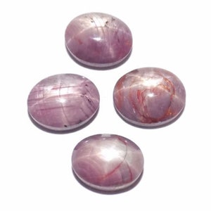 May include: Four oval-shaped, polished gemstones in varying shades of pink and purple are displayed against a white background. Each stone has a star-like effect, with lines radiating from a central point, creating a unique visual appeal.