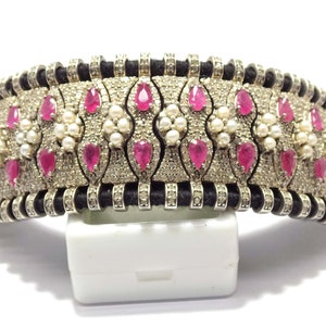 May include: A silver-toned choker necklace with a black cord base. The necklace features alternating sections of small white stones, pink teardrop-shaped stones, and small white pearls. The design is symmetrical and ornate.