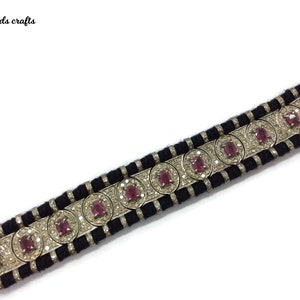 May include: A black and silver bracelet with a repeating pattern of red gemstones and clear crystals. The bracelet has a woven black band and is labeled "India beads crafts".