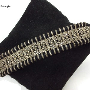 Peut inclure: Un collier ras du cou noir avec un motif argenté orné. Le collier présente une rangée centrale de pierres scintillantes et est présenté sur une surface noire. Le texte "India beads crafts" est dans le coin supérieur gauche.