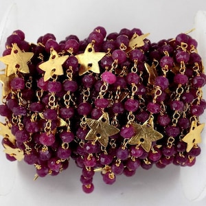 Puede incluir: Una cadena de cuentas con cuentas facetadas de color rojo intenso y dijes de estrella dorados. La cadena está enrollada en una bobina blanca. Las cuentas tienen aproximadamente 3 mm de diámetro.