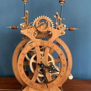May include: A wooden clock with intricate gears and a Roman numeral face. The clock is made of light and dark wood and has a black metal pendulum.
