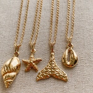 May include: Four gold-colored necklaces with ocean-themed pendants. The pendants include a seashell, starfish, mermaid tail, and a cowrie shell. Each necklace has a delicate chain and a lobster clasp.