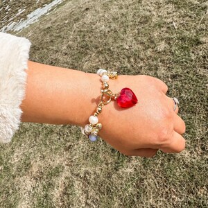 May include: A gold bracelet with white pearls, blue and gold beads, and a red heart charm.