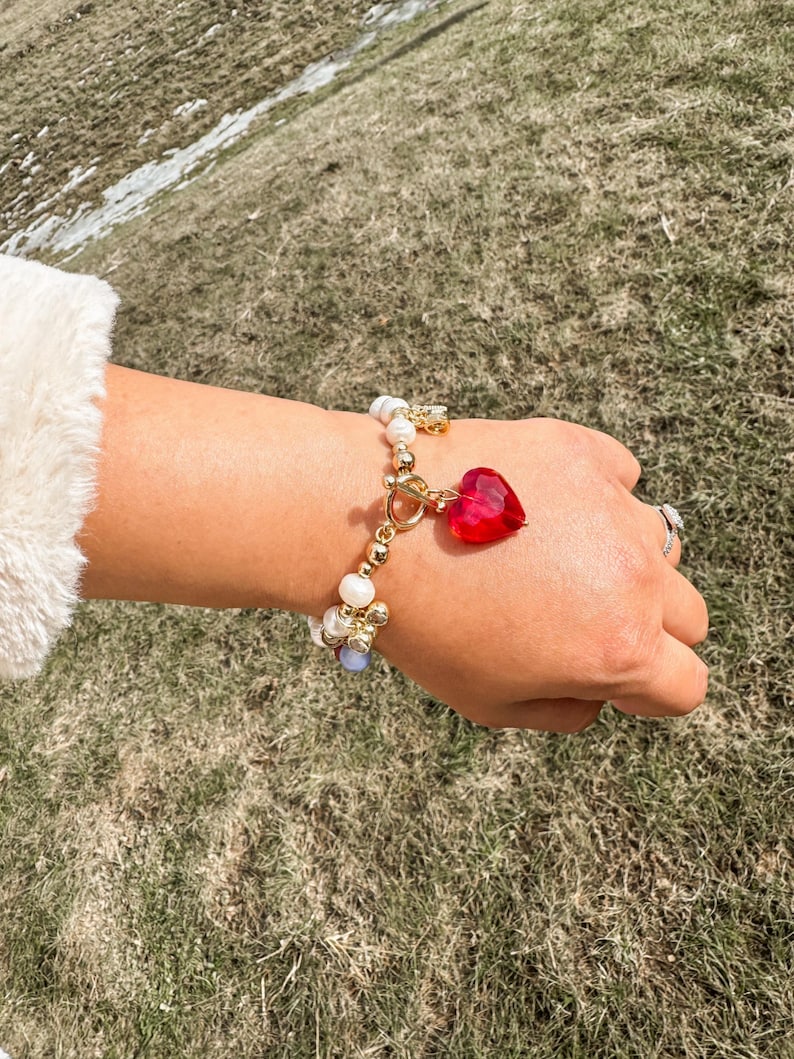 May include: A gold bracelet with white pearls, blue and gold beads, and a red heart charm.