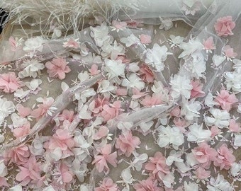May include: Pink and white floral lace fabric with 3D flower embellishments. The fabric has a delicate, sheer texture and is perfect for adding a touch of elegance to any project.