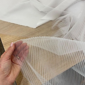 May include: White sheer fabric with horizontal stripes. The fabric is pleated and has a delicate, airy texture.
